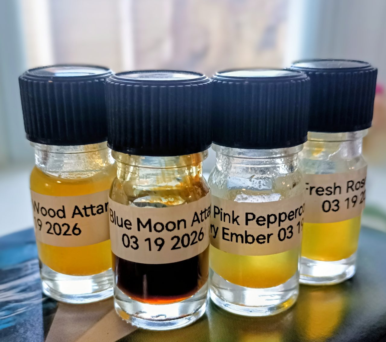 Four small sample vials with handwritten labels and black caps, containing amber and clear liquids