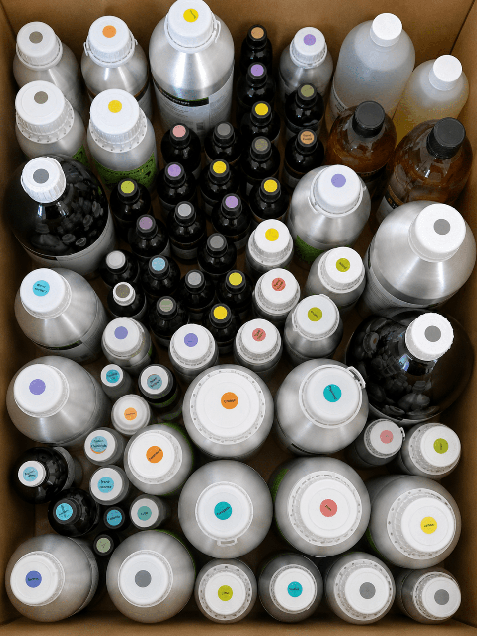 Cardboard box filled with assorted labelled bottles and jugs of liquid chemicals